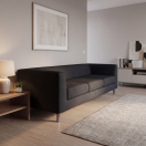 Sofá de oficina moderno de tres cuerpos tapizado en cuero negro, con diseño minimalista de líneas rectas y patas metálicas, ubicado en sala de estar o recepción con muebles de madera, ideal para oficinas, salas de espera y espacios corporativos en Chile.
