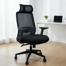 Silla ejecutiva Montreal de color negro con respaldo de malla y cabezal, ubicada en una oficina moderna con escritorio blanco y laptop.