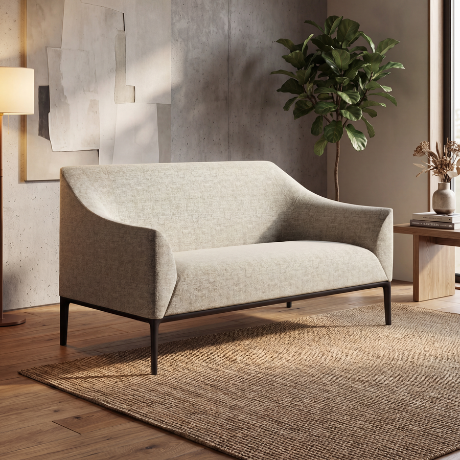 Sofá de oficina moderno de dos cuerpos en color beige claro, tapizado en tela texturizada, con diseño minimalista de líneas curvas y patas metálicas negras delgadas. Ubicado en un ambiente interior elegante con piso de madera, alfombra natural, mesa lateral con decoración y planta verde, ideal para salas de espera, recepción o espacios corporativos en Chile.