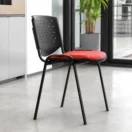 Silla de Visita Prisma con estructura metálica negra, respaldo perforado y asiento tapizado rojo en oficina moderna luminosa.