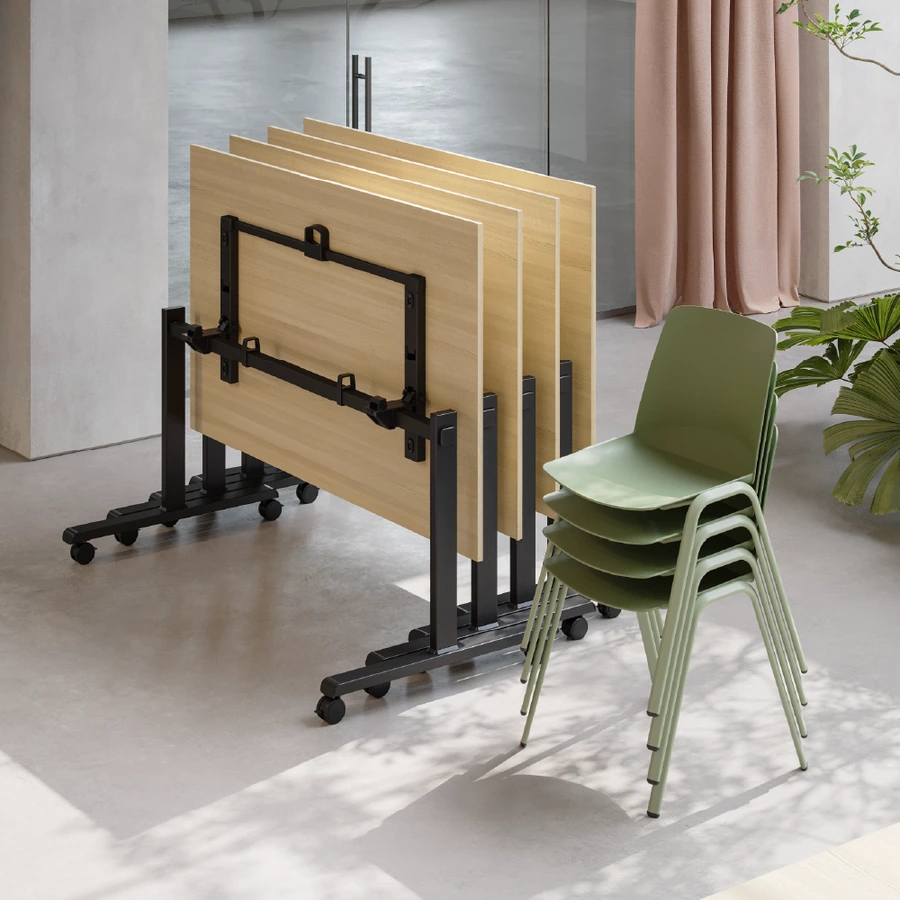 Mesas con estructura abatible Match plegadas junto a sillas apilables en una oficina