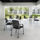 Sillas de Visita Jazz negras con ruedas en un espacio de coworking con mesas blancas y ventanales
