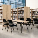 Sillas de Visita Meta negras apilables en torno a una mesa de madera en una biblioteca corporativa