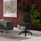 Silla de cajero Romy negra en un puesto de trabajo alto junto a un mueble de madera