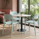 Sillas de terraza Klint verde agua en torno a una mesa de terrazo en una cafeteria con ventanal